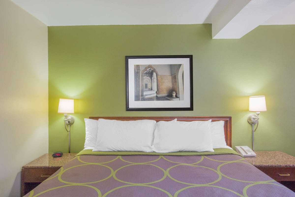 A hotel room with a bed, two bedside lamps, a framed picture on the wall, and a nightstand with a phone.