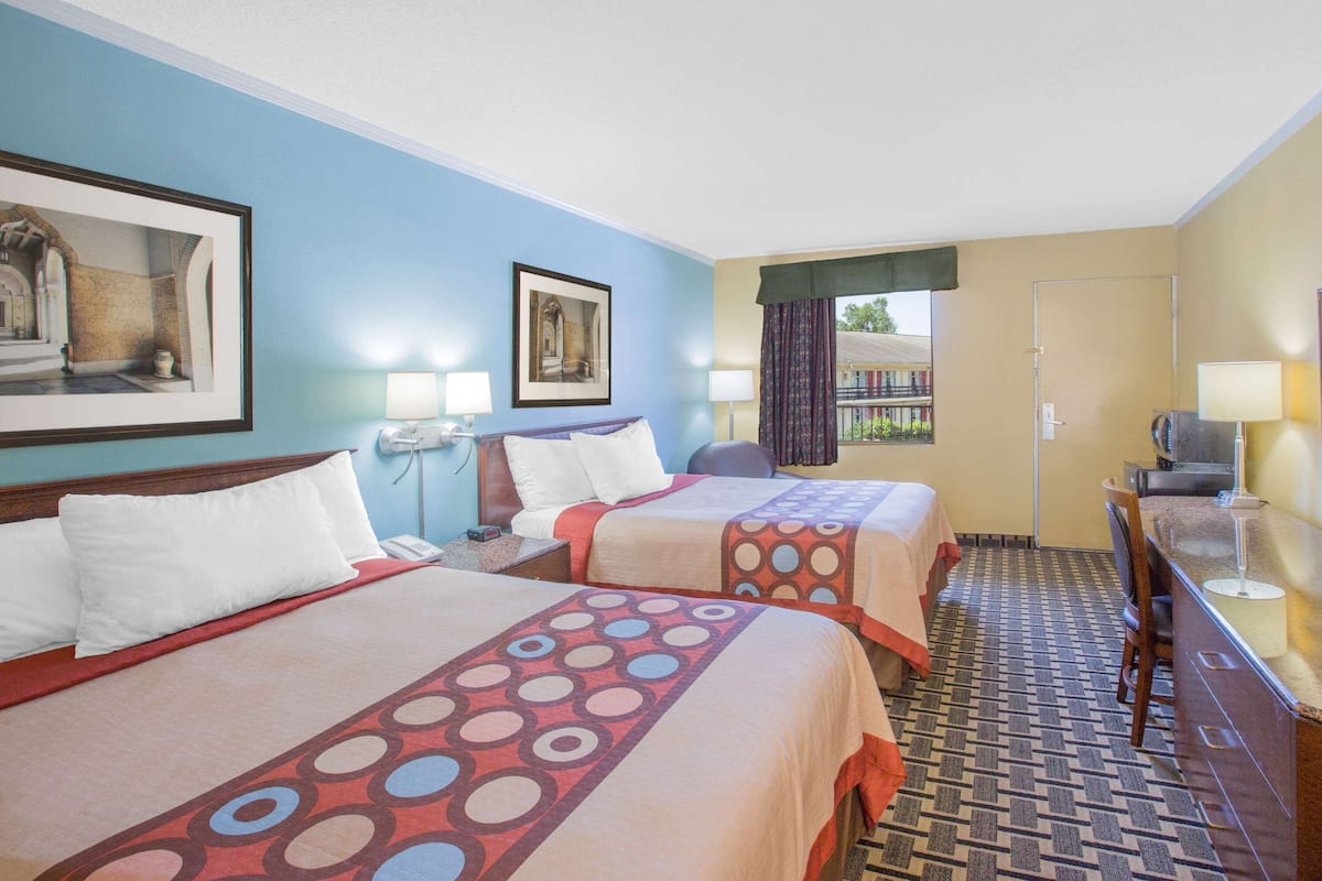 A hotel room with two beds, a desk, a chair, a TV, and a balcony with a view.