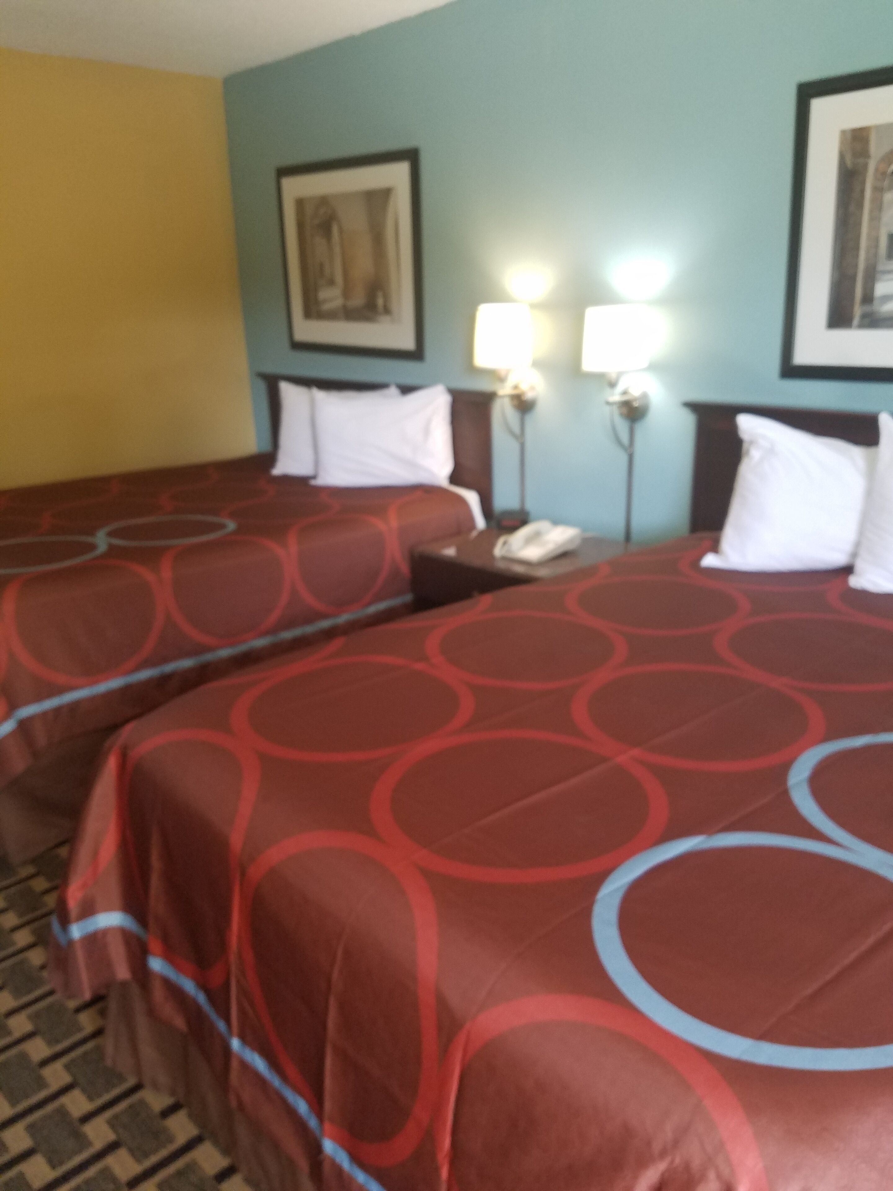 Habitación de hotel con dos camas, cada una con ropa de cama roja y almohadas blancas. Hay dos lámparas de noche, un cuadro en la pared y un teléfono en la mesita de noche.