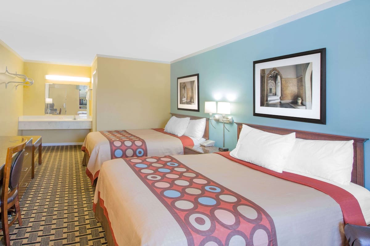 A hotel room with two beds, a desk, a chair, a mirror, and artwork on the walls.