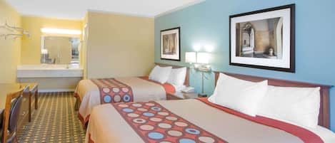 Ein Hotelzimmer mit zwei Betten, einem Schreibtisch, einem Stuhl, einem Spiegel und Bildern an den Wänden.