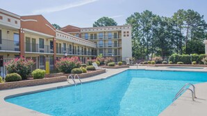 A swimming pool with a clear blue water, surrounded by a brick walkway and a row of buildings with balconies and windows. - Super 8 by Wyndham Jasper (Jasper)