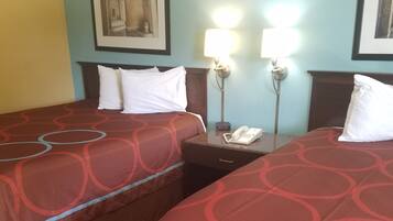 Ett hotellrum med två sängar, var och en med ett rött överkast och vita kuddar. Det finns ett nattduksbord med en lampa och en telefon på. Väggarna är målade i ljusblått och gult, och det hänger en inramad tavla på väggen.