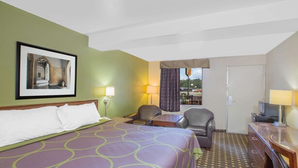 A hotel room with a large bed, two chairs, a desk, and a television. - Super 8 by Wyndham Jasper (Jasper)