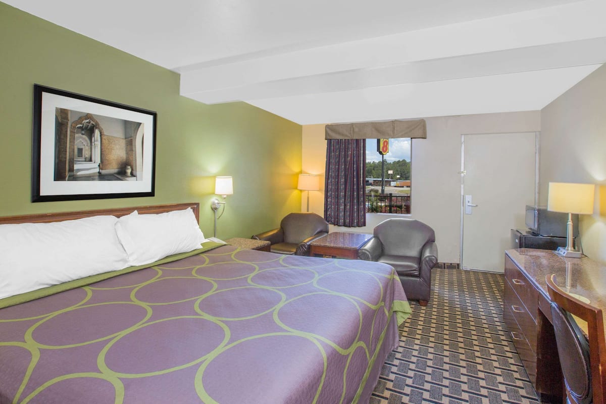 A hotel room with a large bed, two chairs, a desk, and a television.