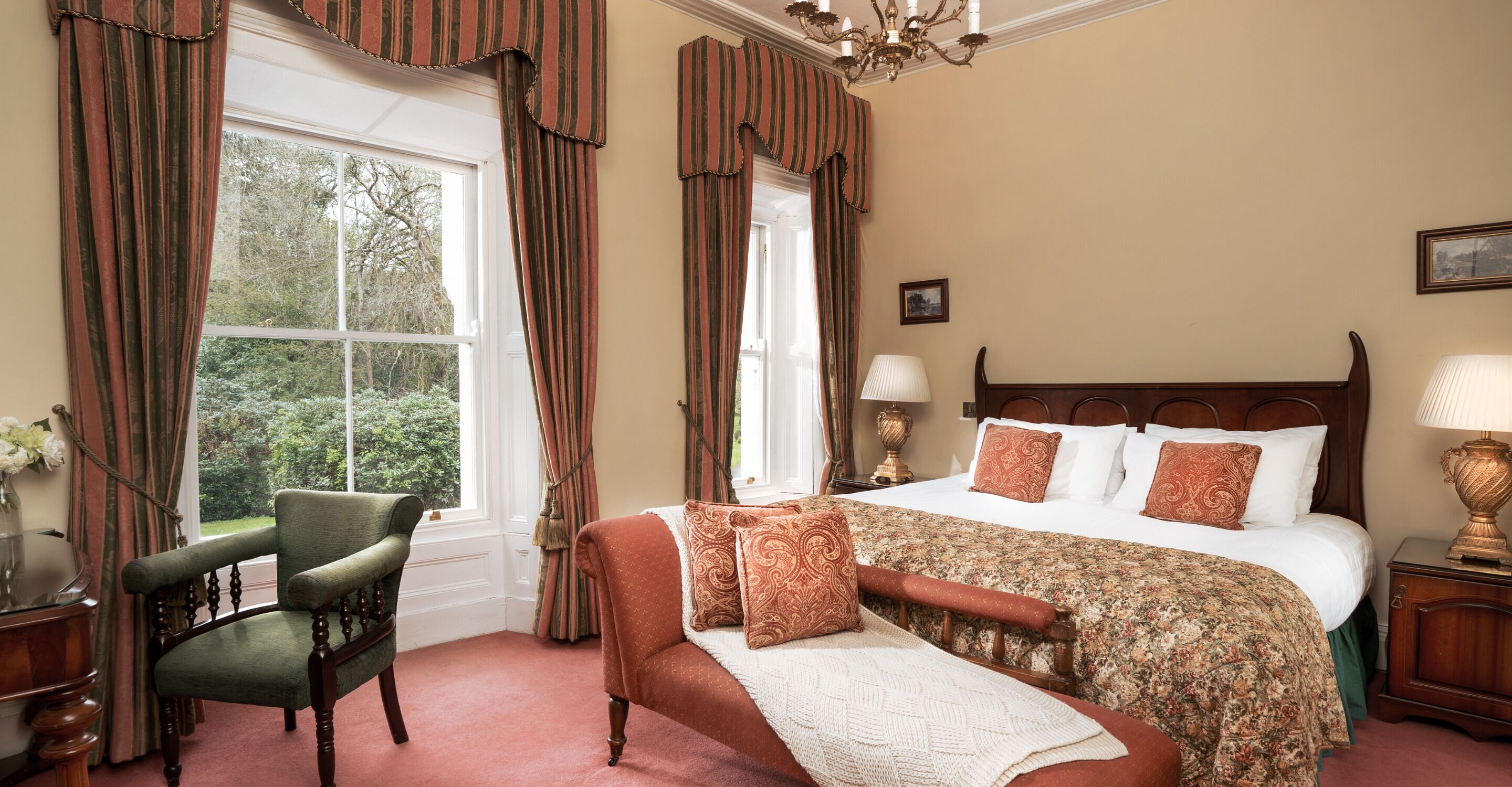 A bedroom with a large bed, a chair, a nightstand, and a window with curtains.