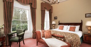 A bedroom with a large bed, a chair, a nightstand, and a window with curtains. - Beech Hill Country House Hotel (Londonderry)