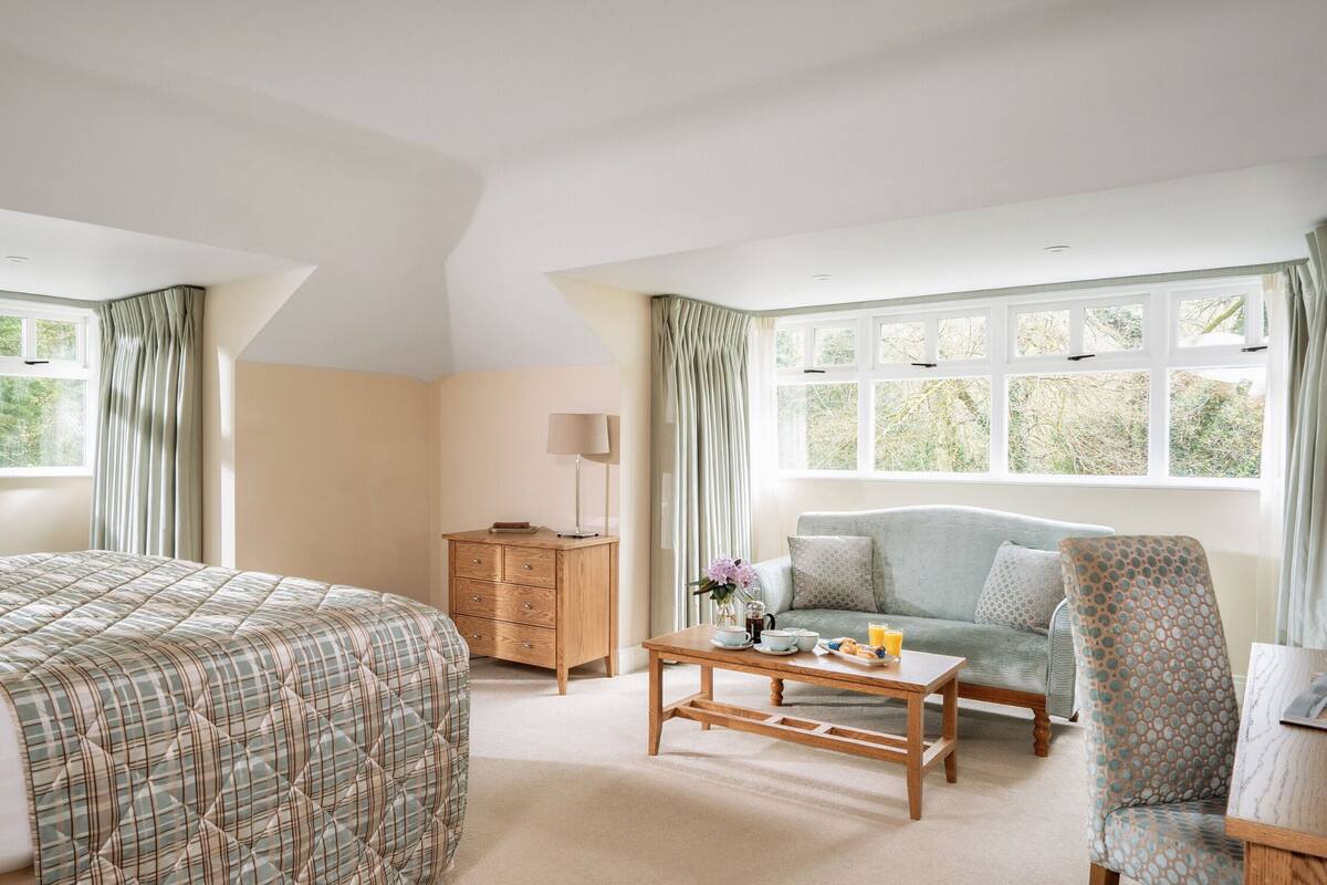A bedroom with a bed, a wooden dresser, a sofa, a chair, and a table with breakfast items.