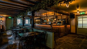 A bar area with wooden tables and chairs, a bar counter with glasses, and a brick wall.