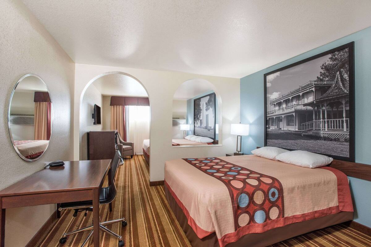 A hotel room with a bed, desk, chair, and two mirrors.