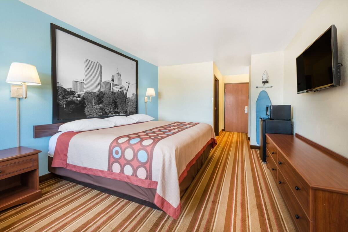 A hotel room with a bed, a television, a desk, and a wall-mounted TV.