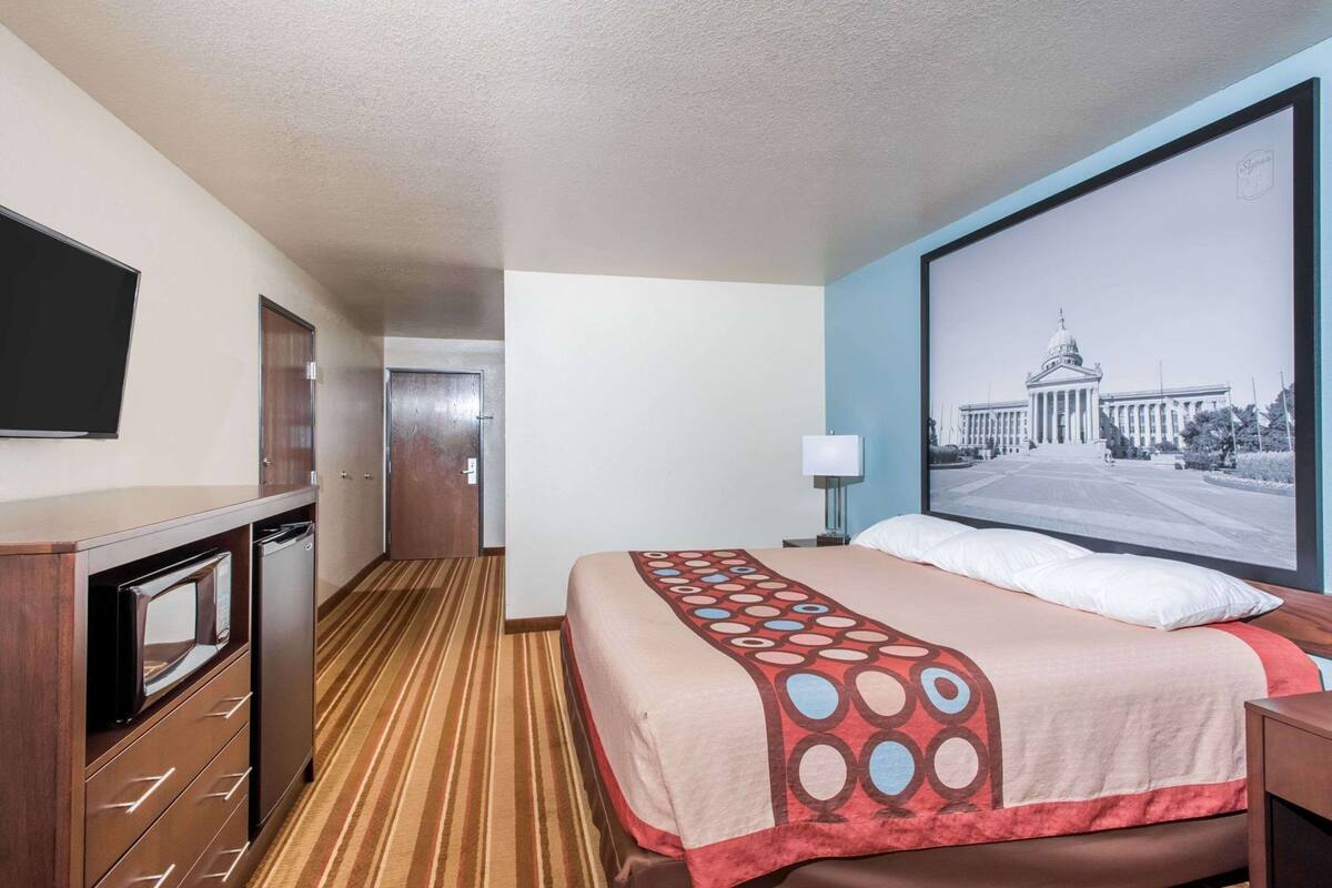 A hotel room with a bed, a television, a desk with a microwave, and a door leading to another room.