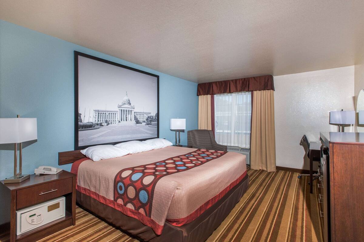 A hotel room with a large bed, a desk with a lamp, a chair, and a large framed picture on the wall.
