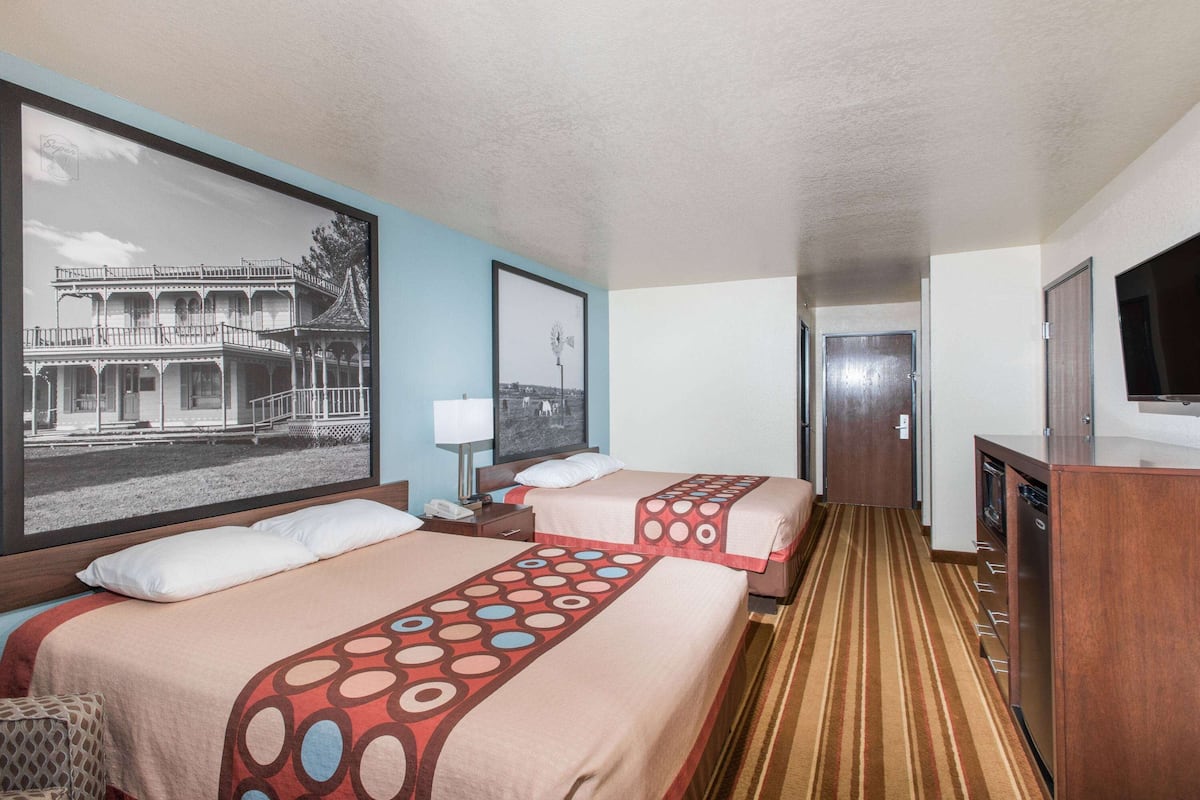 A hotel room with two beds, a large framed picture of a building, a television, and a wooden cabinet.