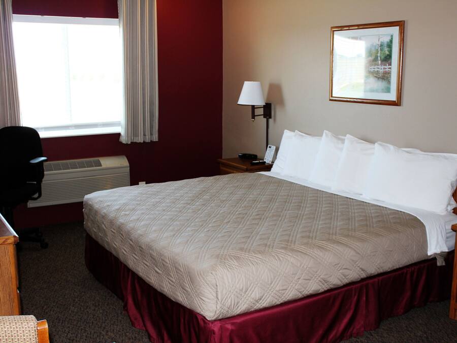 A hotel room with a large bed, a desk, a chair, a lamp, and a window with curtains.