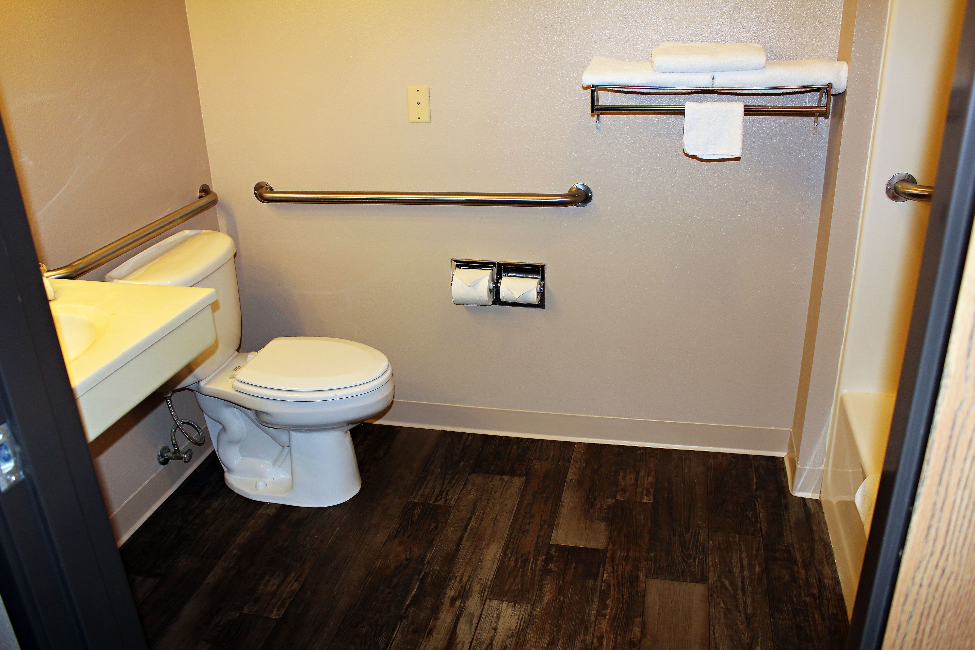 Ein kleines, modernes Badezimmer mit Toilette, Waschbecken und Haltegriffen.