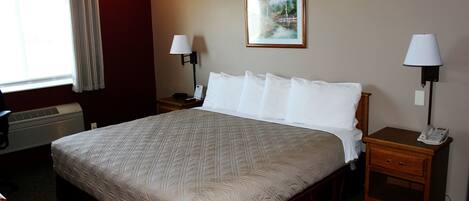 Habitación de hotel con una cama grande, dos mesitas de noche, una lámpara de pared, un cuadro enmarcado y una ventana con cortinas.