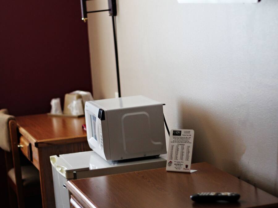 A hotel room with a wooden desk, a microwave, a remote control, and a lamp.