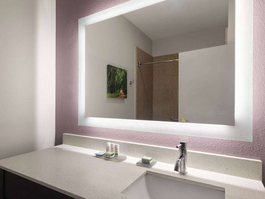A bathroom with a large mirror, a sink with toiletries, and a shower visible in the reflection.