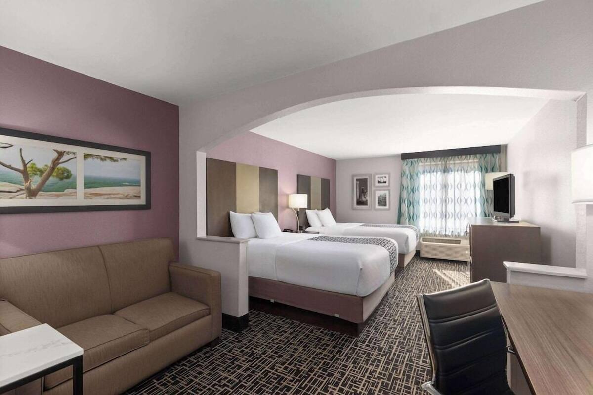 A hotel room with a sofa, two beds, a desk, and a TV.