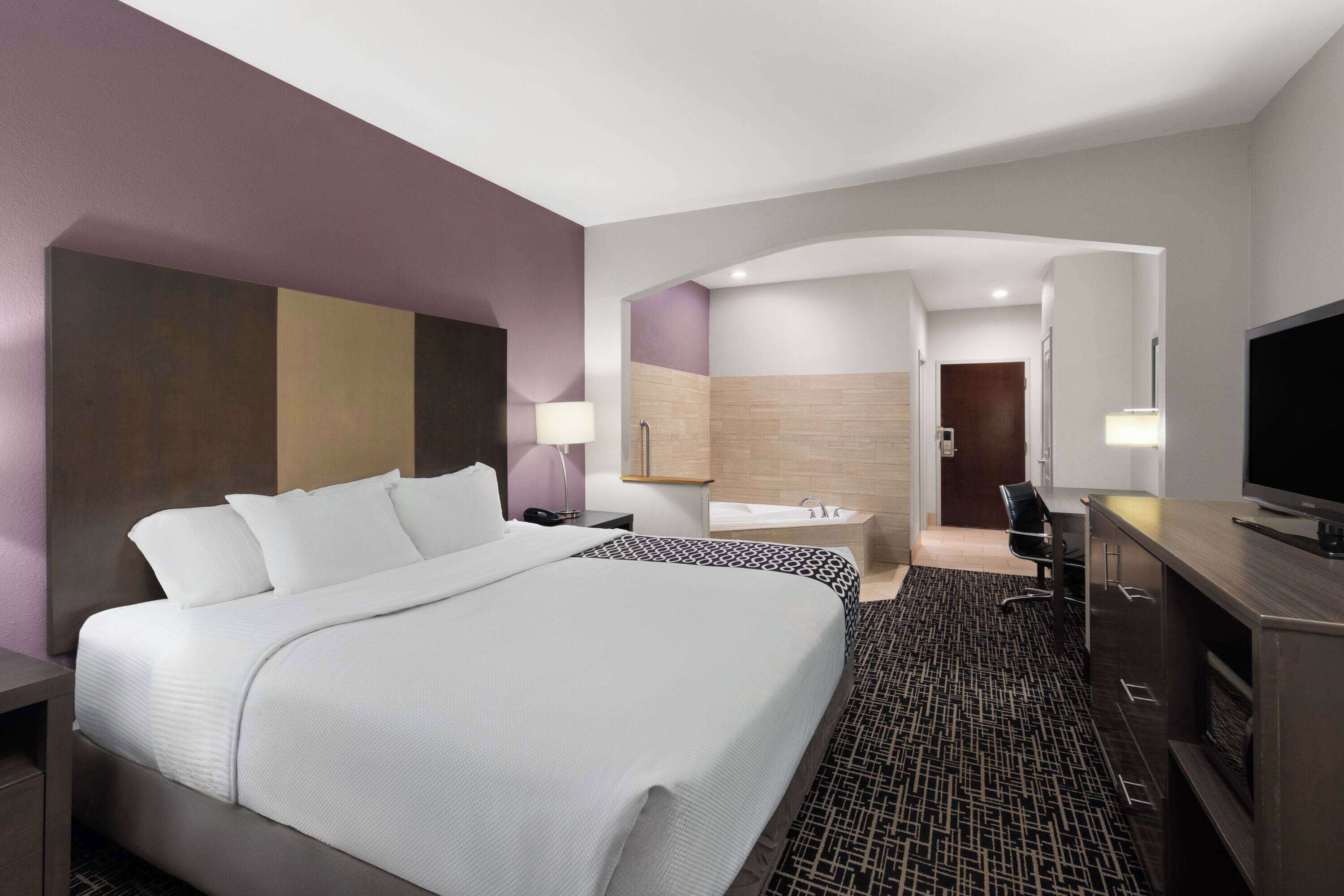 Ein modernes Hotelzimmer mit einem großen Bett, einem Schreibtisch, einem Fernseher und einem Badezimmer mit Badewanne und Dusche.