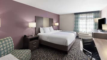 A hotel room with a large bed, a desk, a chair, a TV, and a window with curtains.