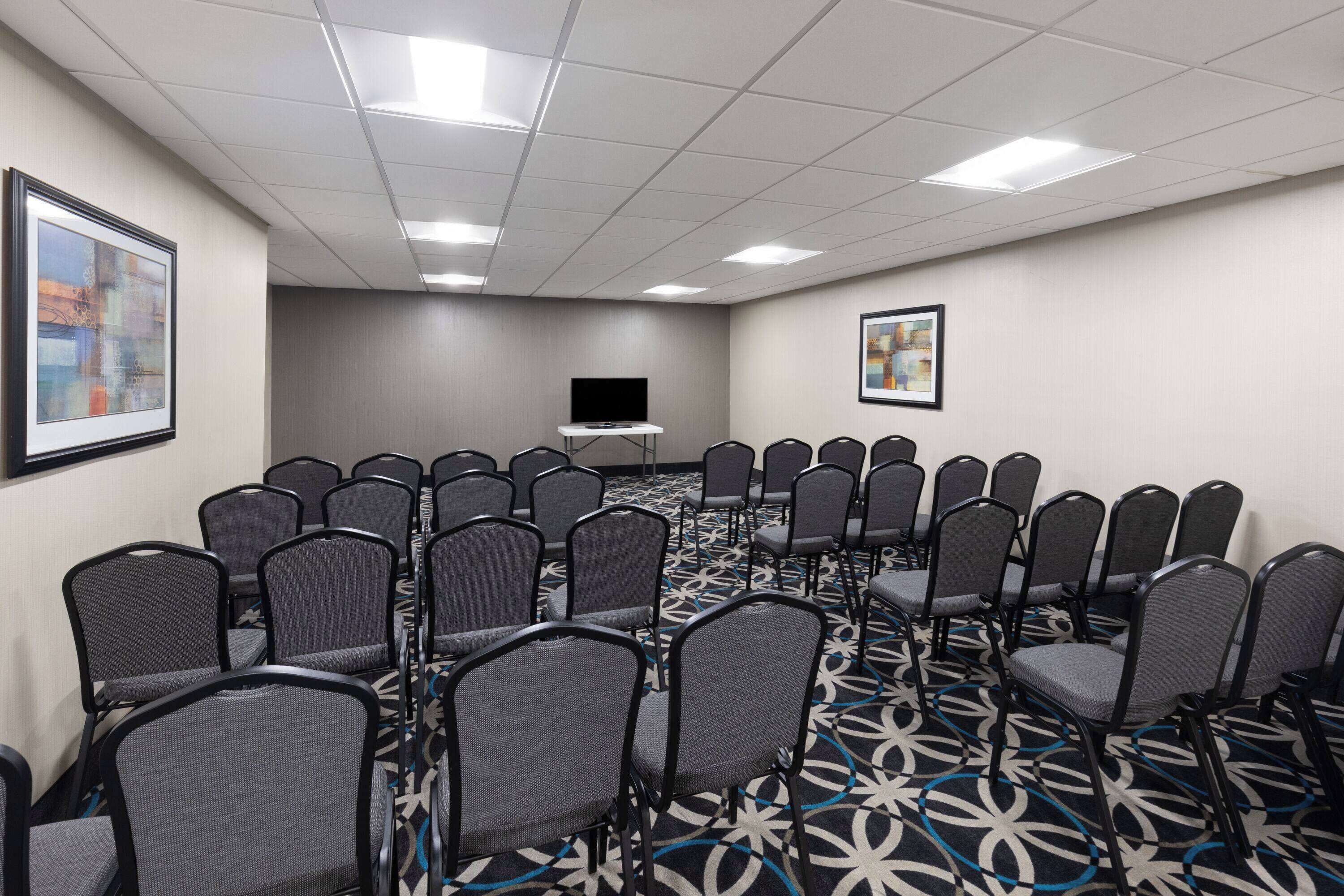 Un salón de conferencias con filas de sillas, una televisión y dos cuadros en las paredes.