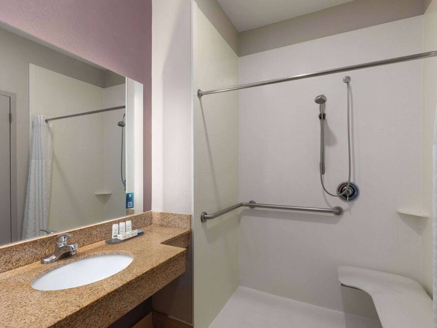 A bathroom with a granite countertop sink, a mirror, a shower with a grab bar, and a white bathtub.