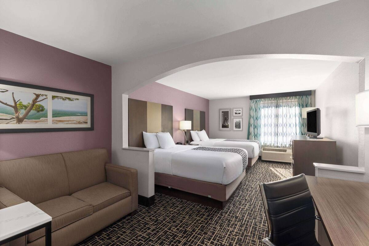 A hotel room with two beds, a sofa, a desk, and a TV.