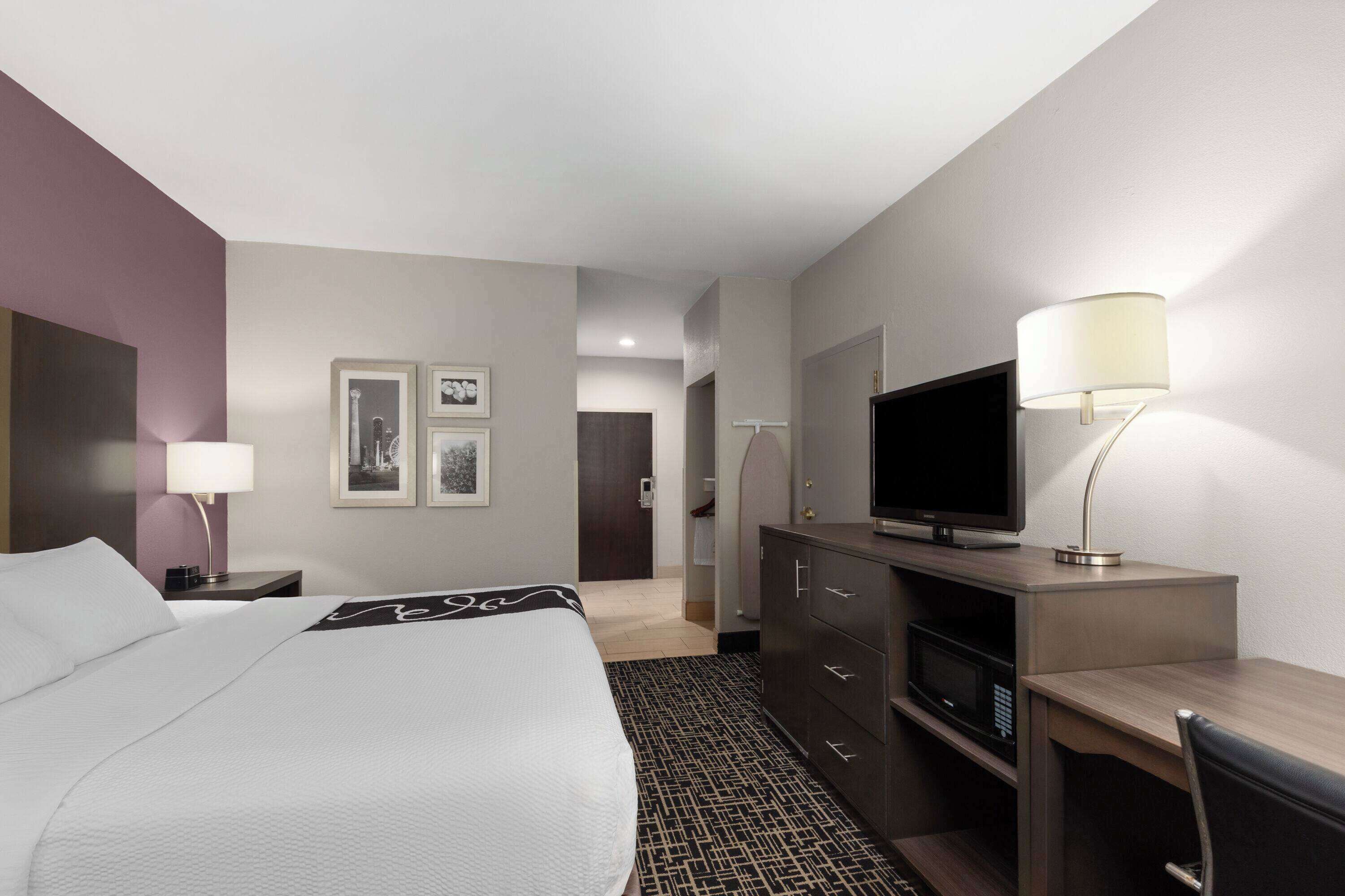 A hotel room with a bed, a desk, a TV, and a lamp.
