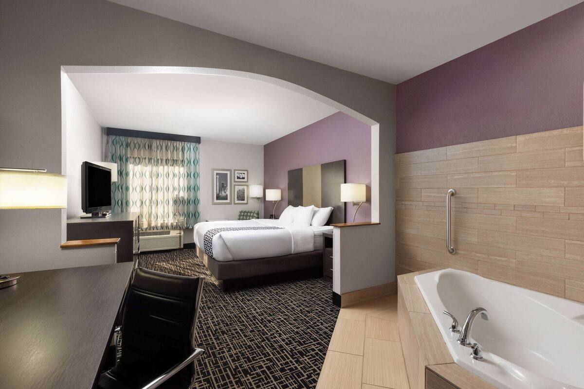 A hotel room with a bed, a desk, a television, a bathroom with a bathtub, and a shower.