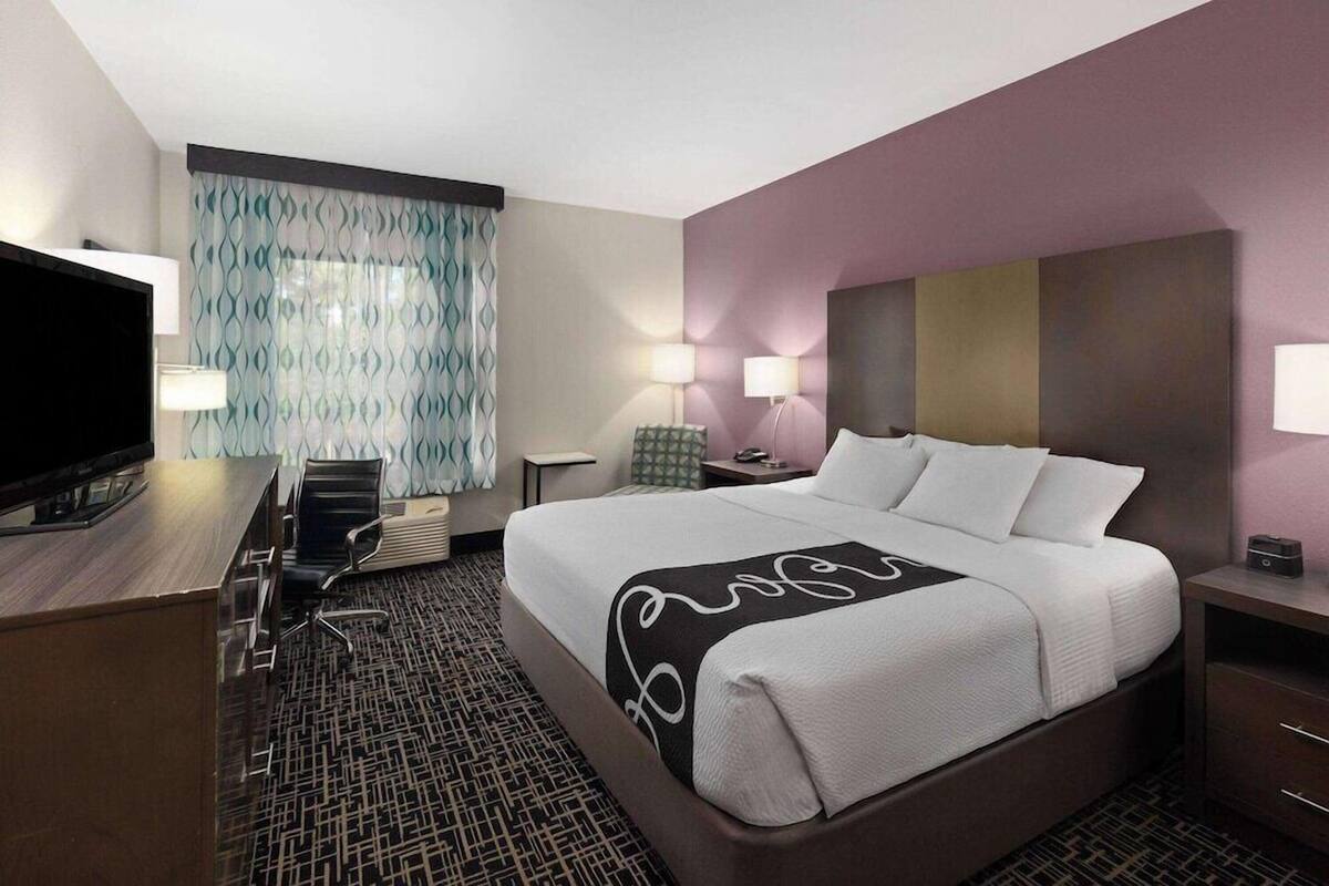 A hotel room with a bed, desk, chair, TV, lamps, and patterned curtains.