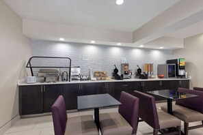 A modern kitchen with dark cabinets, a central island, and a seating area with purple chairs.