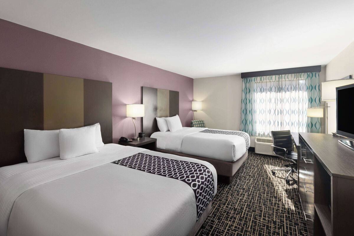 A hotel room with two beds, a desk, and a TV.