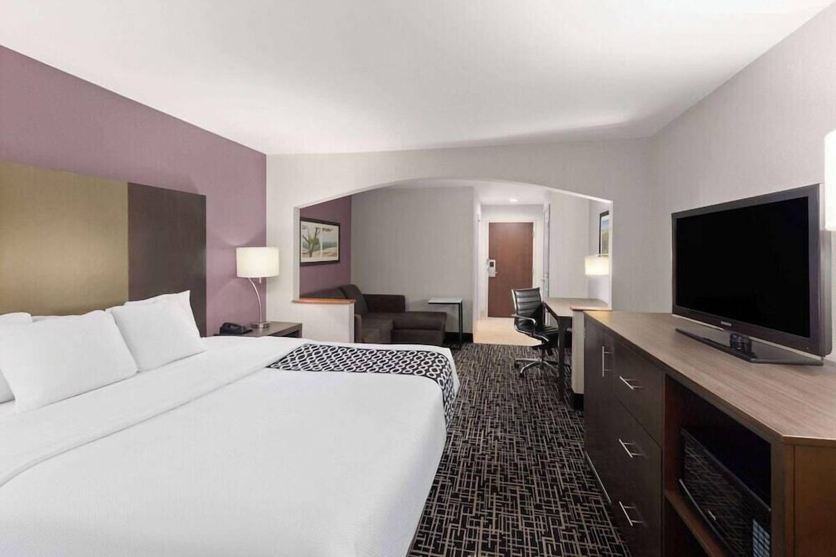A hotel room with a large bed, a desk with a chair, a television, and a small seating area with a couch and a table.