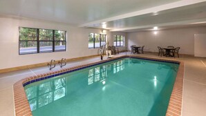 An indoor swimming pool with clear water, surrounded by a tiled deck and equipped with safety railings.