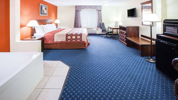Habitación de hotel con cama, dos mesitas de noche con lámparas, un escritorio con silla, televisor y microondas.