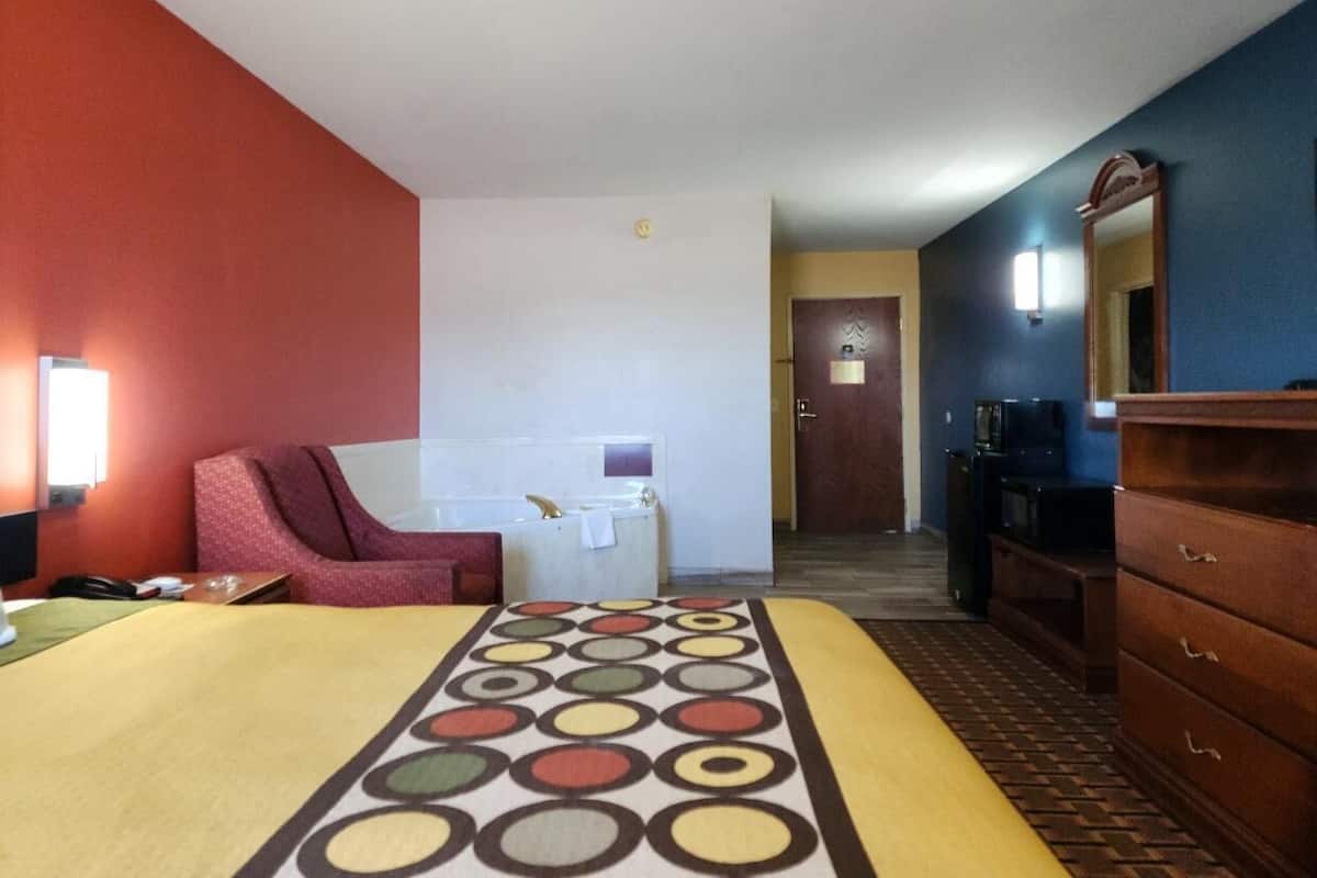 A hotel room with a bed, a red armchair, a small table, a desk, a mirror, and a dresser.