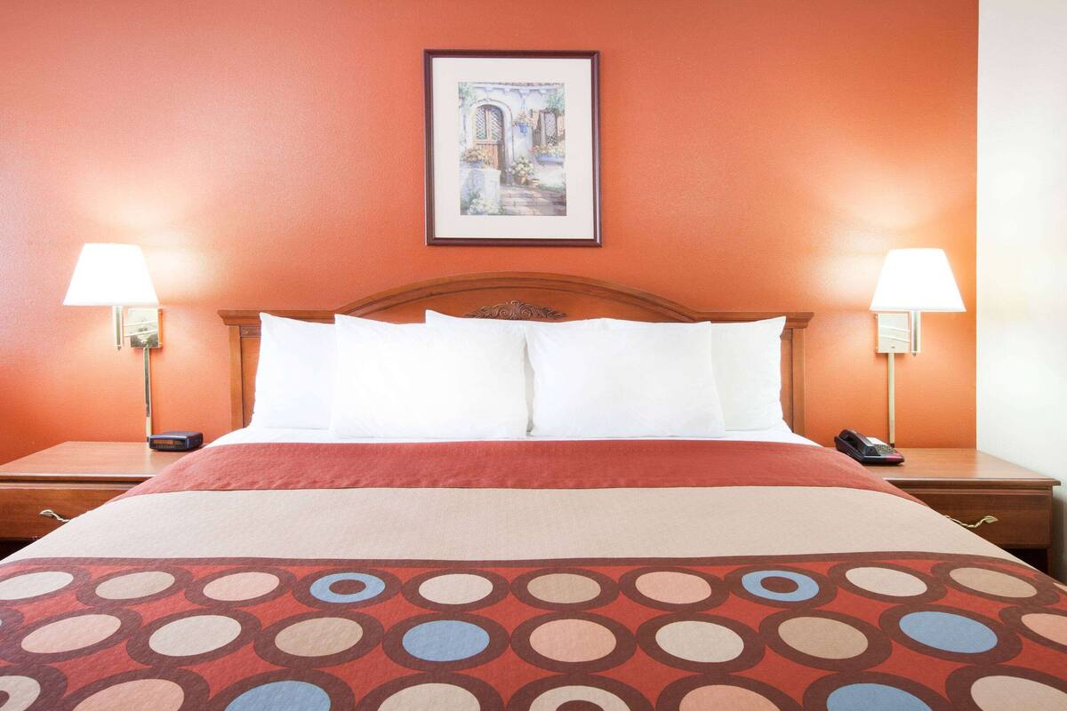 A hotel room with a large bed, two bedside lamps, a framed picture on the wall, and a wooden headboard.