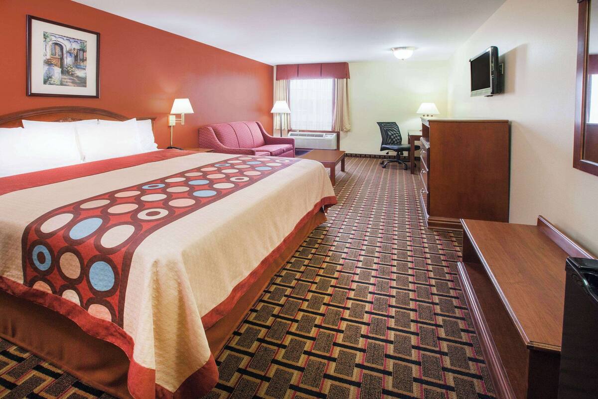A hotel room with a large bed, a desk, a chair, and a television.