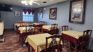 Un comedor con mesas y sillas, un ventilador de techo y cuadros en las paredes.