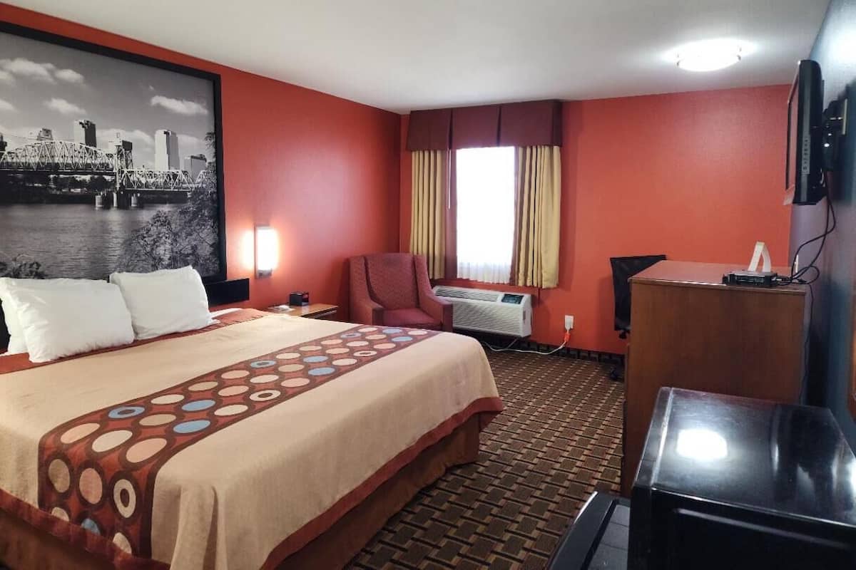 A hotel room with a bed, a desk, a chair, and a large window with curtains.