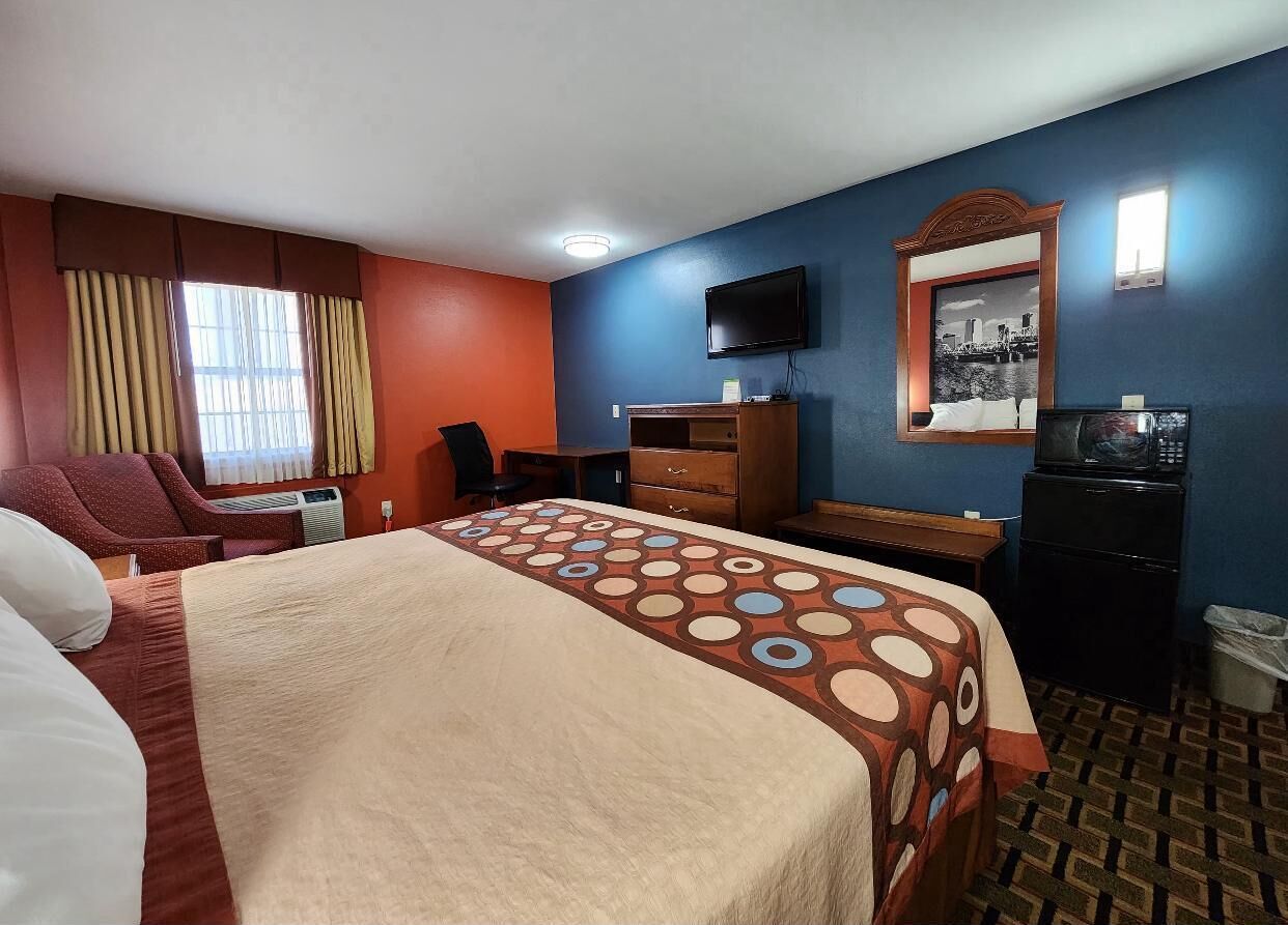 A hotel room with a bed, a desk, a chair, a television, and a mirror.