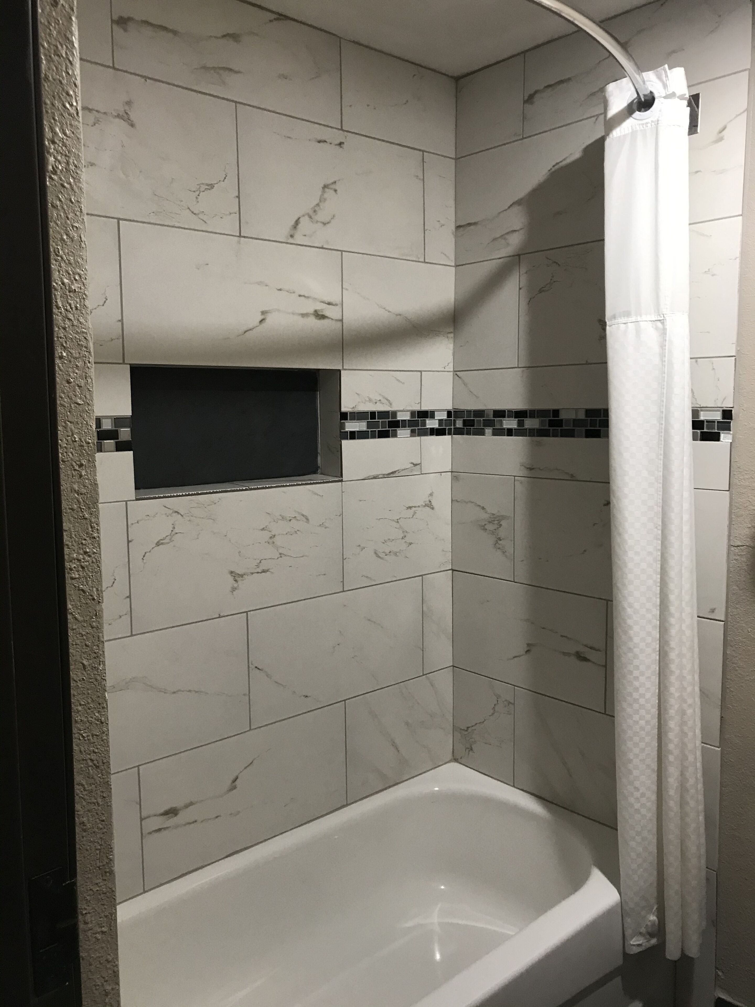 A bathroom with a bathtub, white marble tiles, a black rectangular shelf, and a shower curtain.