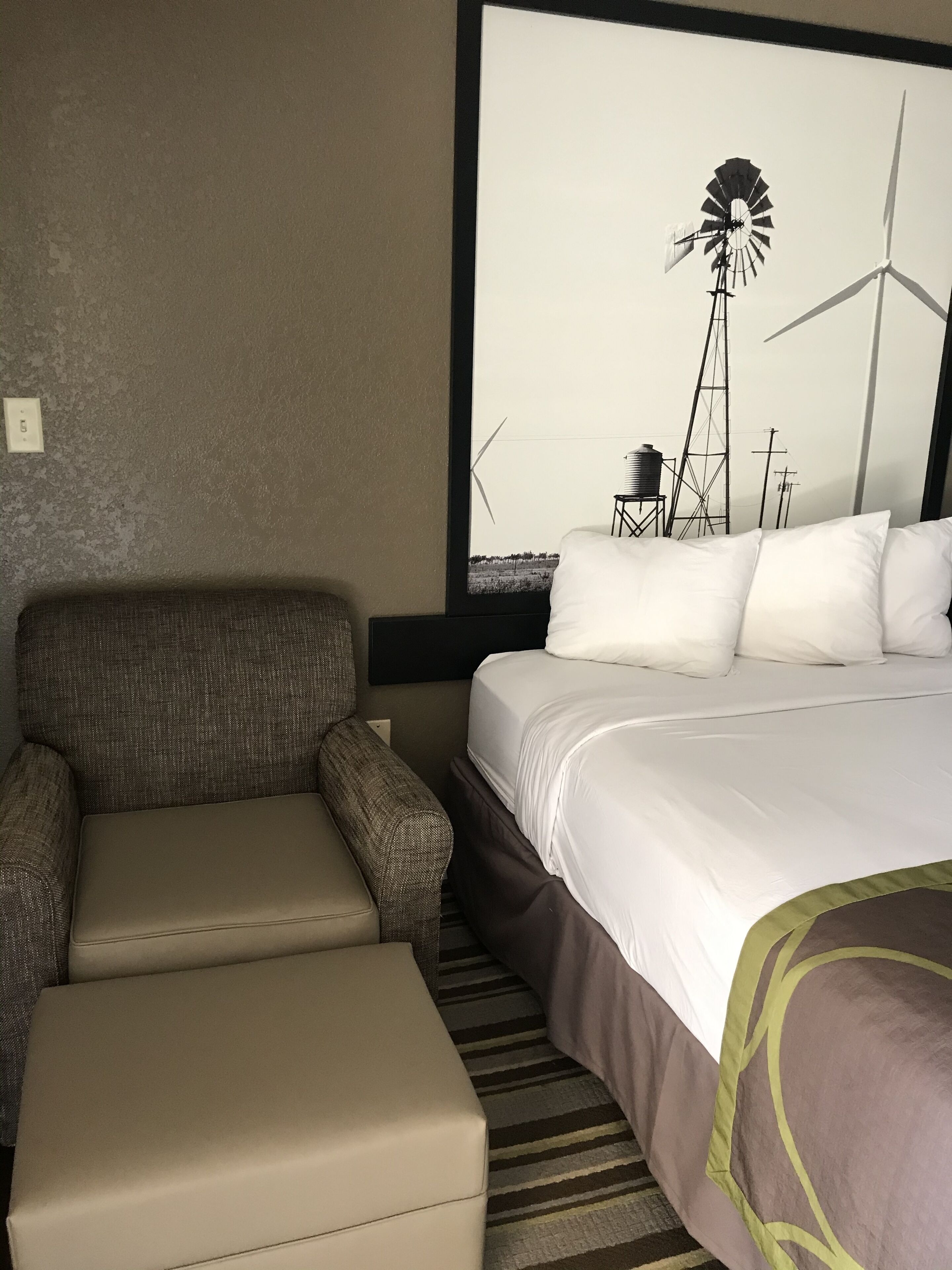 A hotel room with a bed, a chair, and a large window with a view of wind turbines.