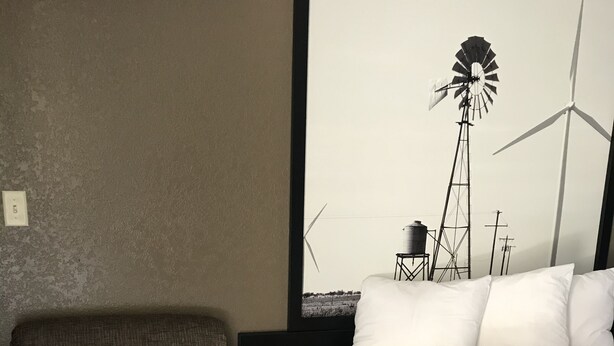Ein Hotelzimmer mit Bett, Sessel und großem Fenster mit Blick auf Windkraftanlagen.