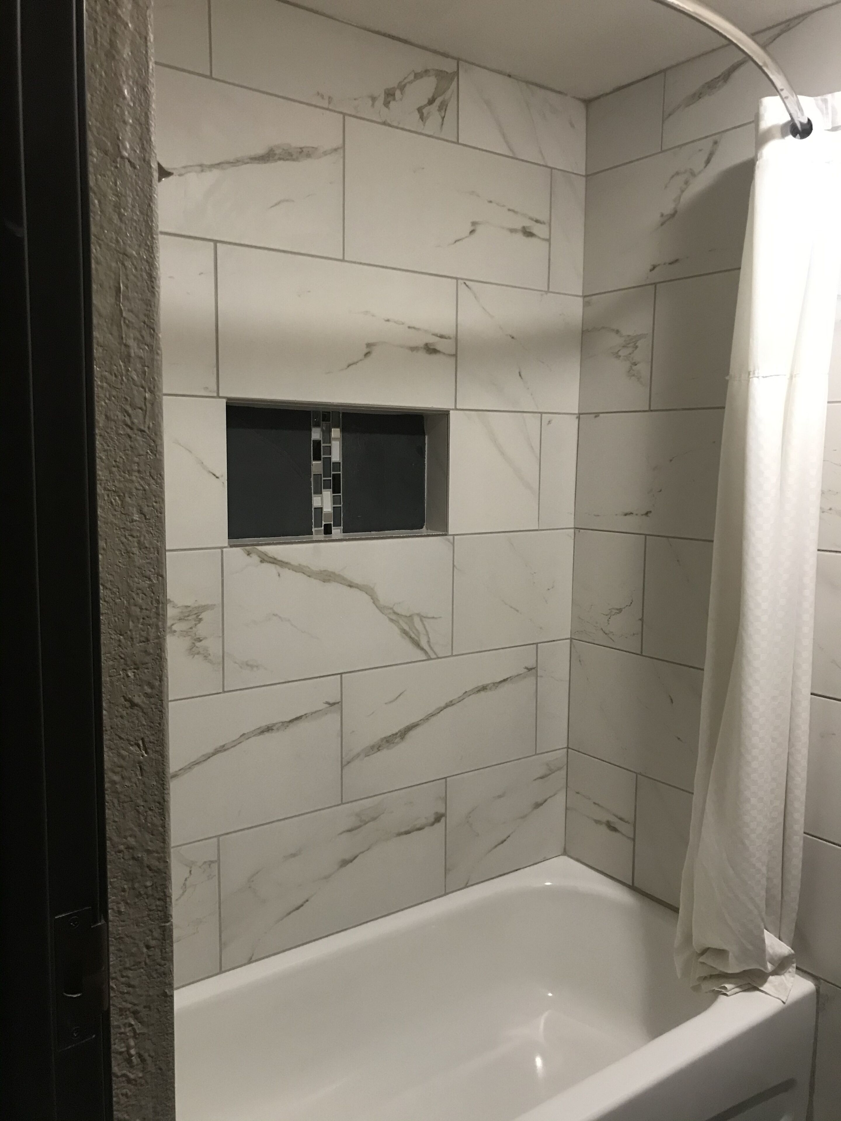 Un baño con una bañera blanca, baldosas de mármol y una cortina de ducha.