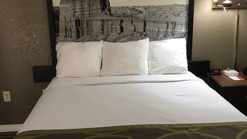 Een hotelkamer met een groot bed, een hoofdeinde met een print van een rotsformatie, een nachtkastje met een lamp en een stopcontact.