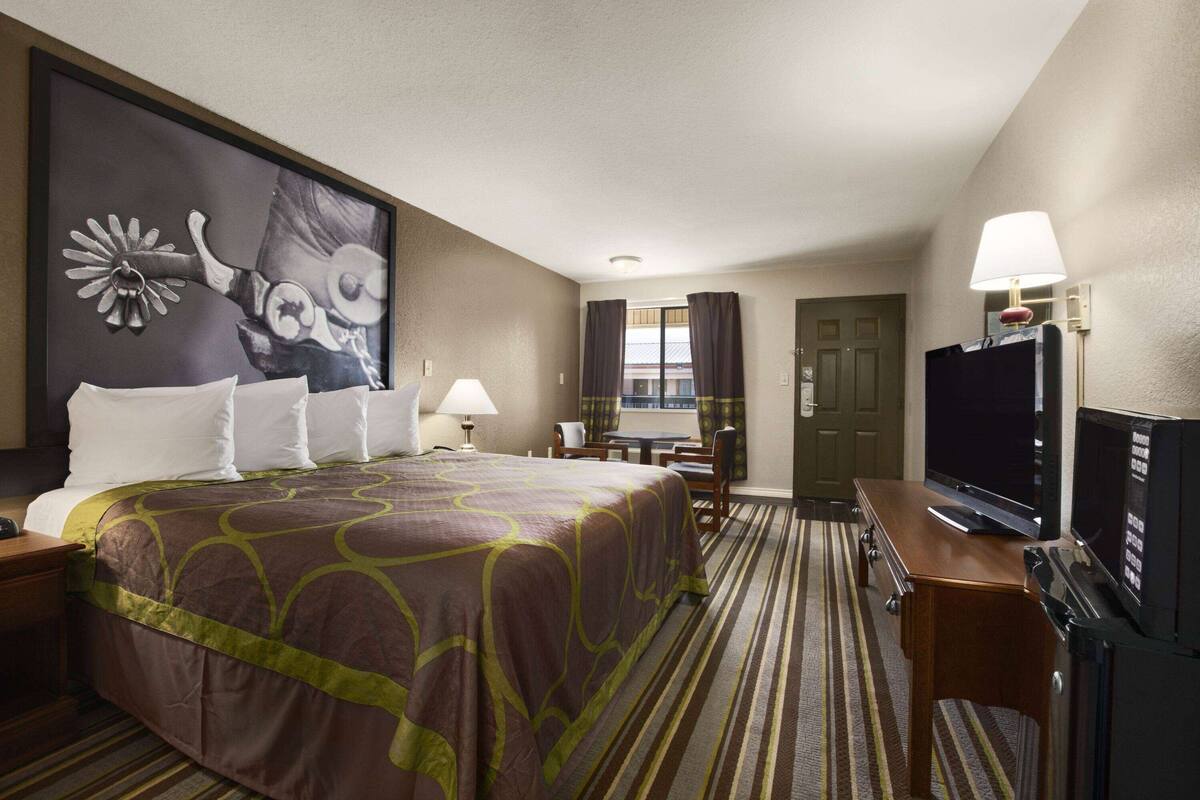 Ein Hotelzimmer mit einem großen Bett, einem Fernseher, einem Schreibtisch mit Lampe und einem Bild an der Wand.