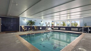 Une piscine intérieure avec un mur carrelé, un poste de surveillance pour le sauveteur et une fenêtre donnant sur les arbres.